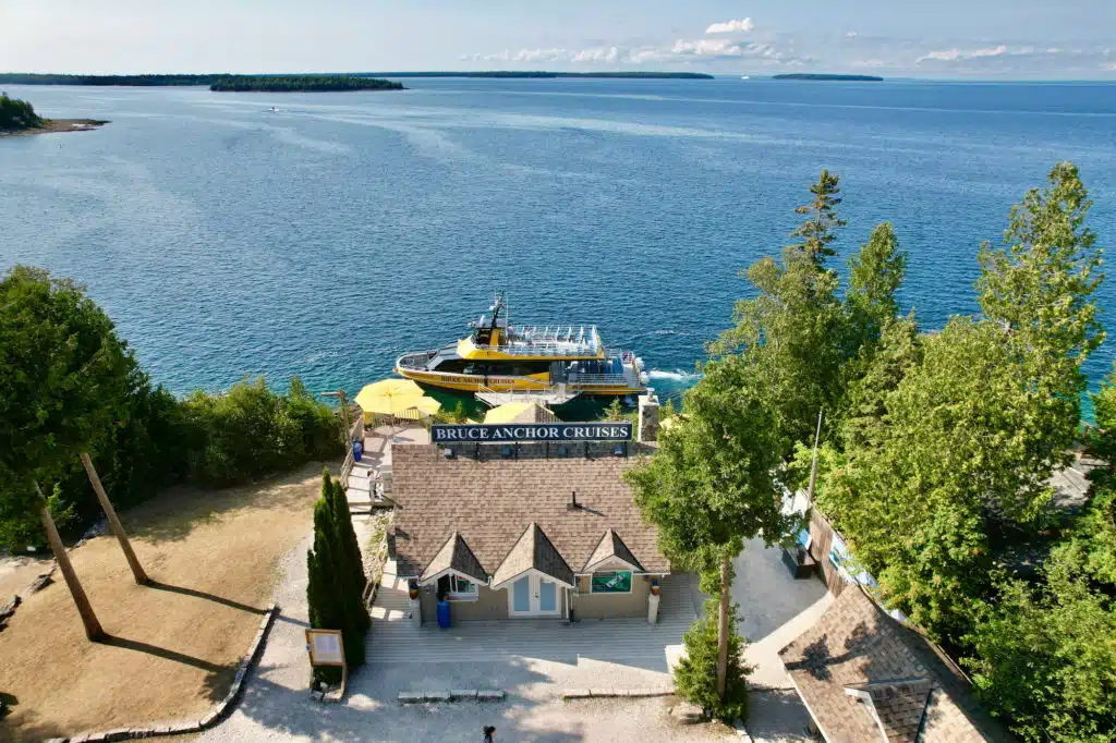A scenic view of Bruce Anchor Cruises dock, turquoise water, lush trees, and a docked, colorful tour boat under a clear blue sky.